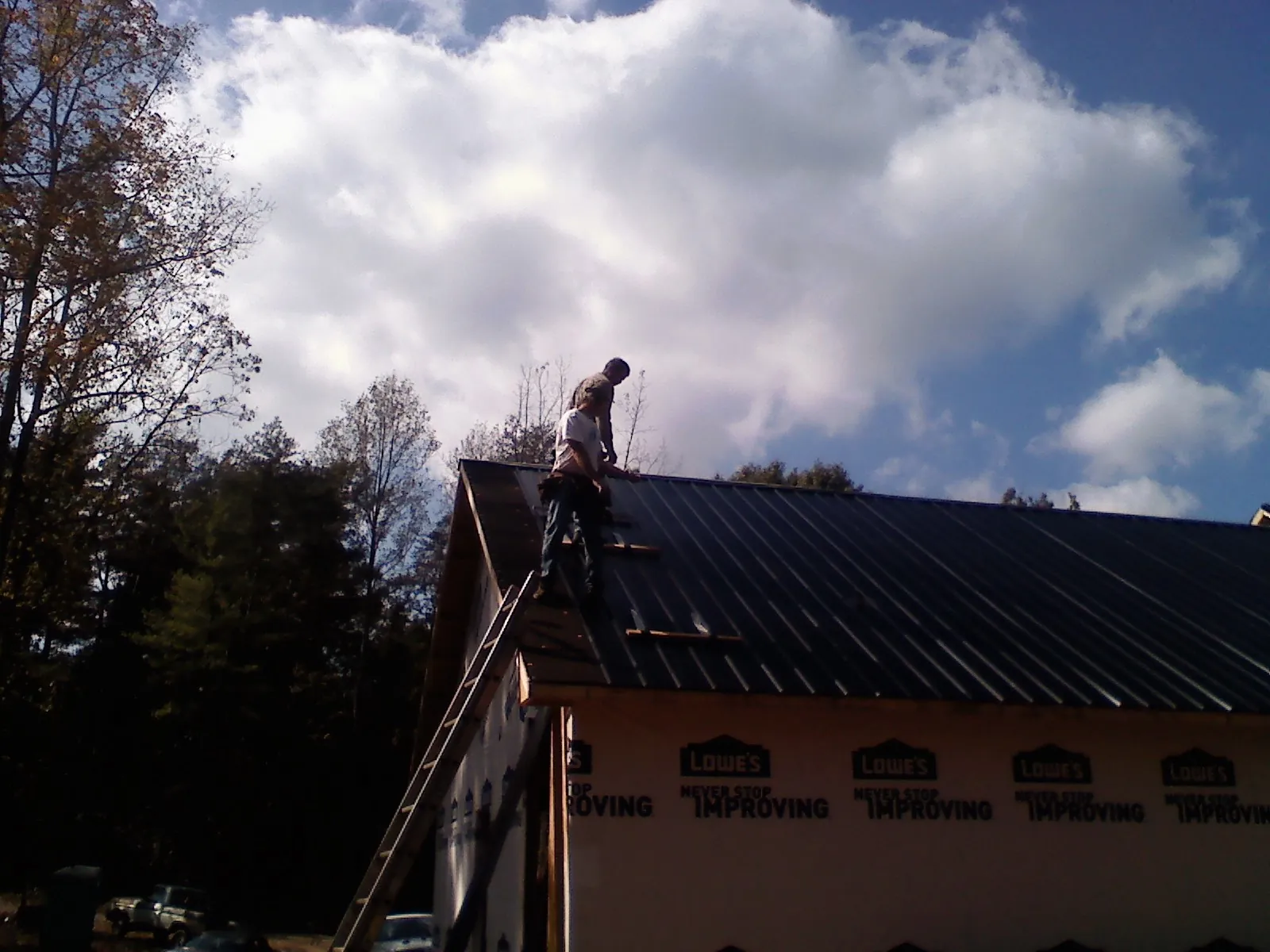 Roofer fastening dark metal panels high against a cloudy sky, from a Roof Inspection job in Ashby