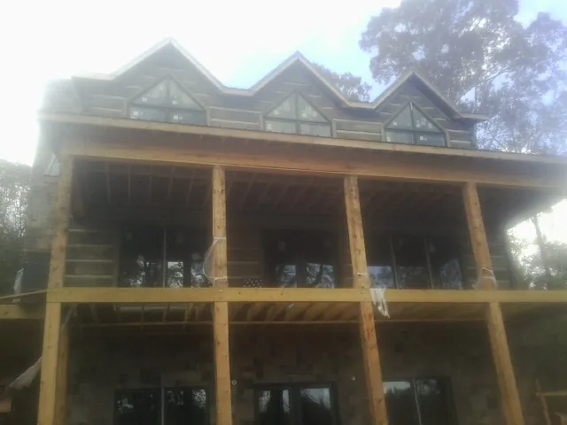 Dormers and porch framing on a large log home under construction — Roof Coating work by our crew in Ashby