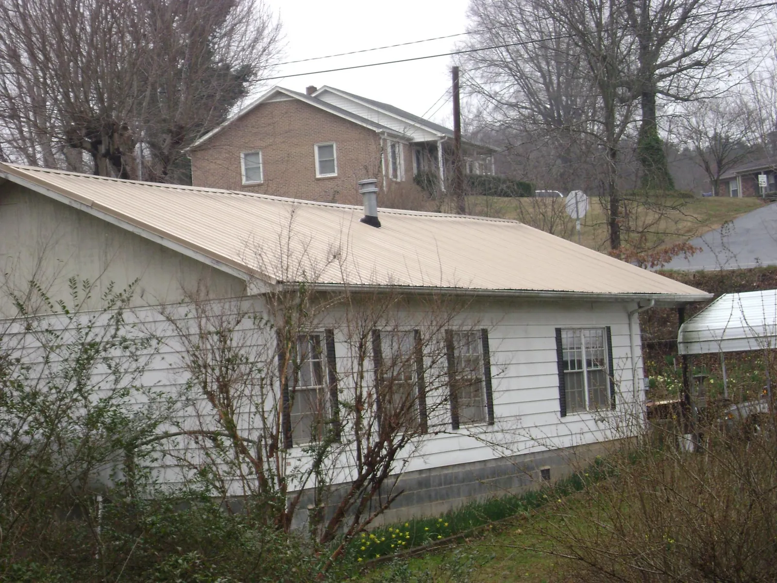 Tan metal roof on a white sided house set into a hillside — Commercial Roofing by Roofing Brothers in Ashby