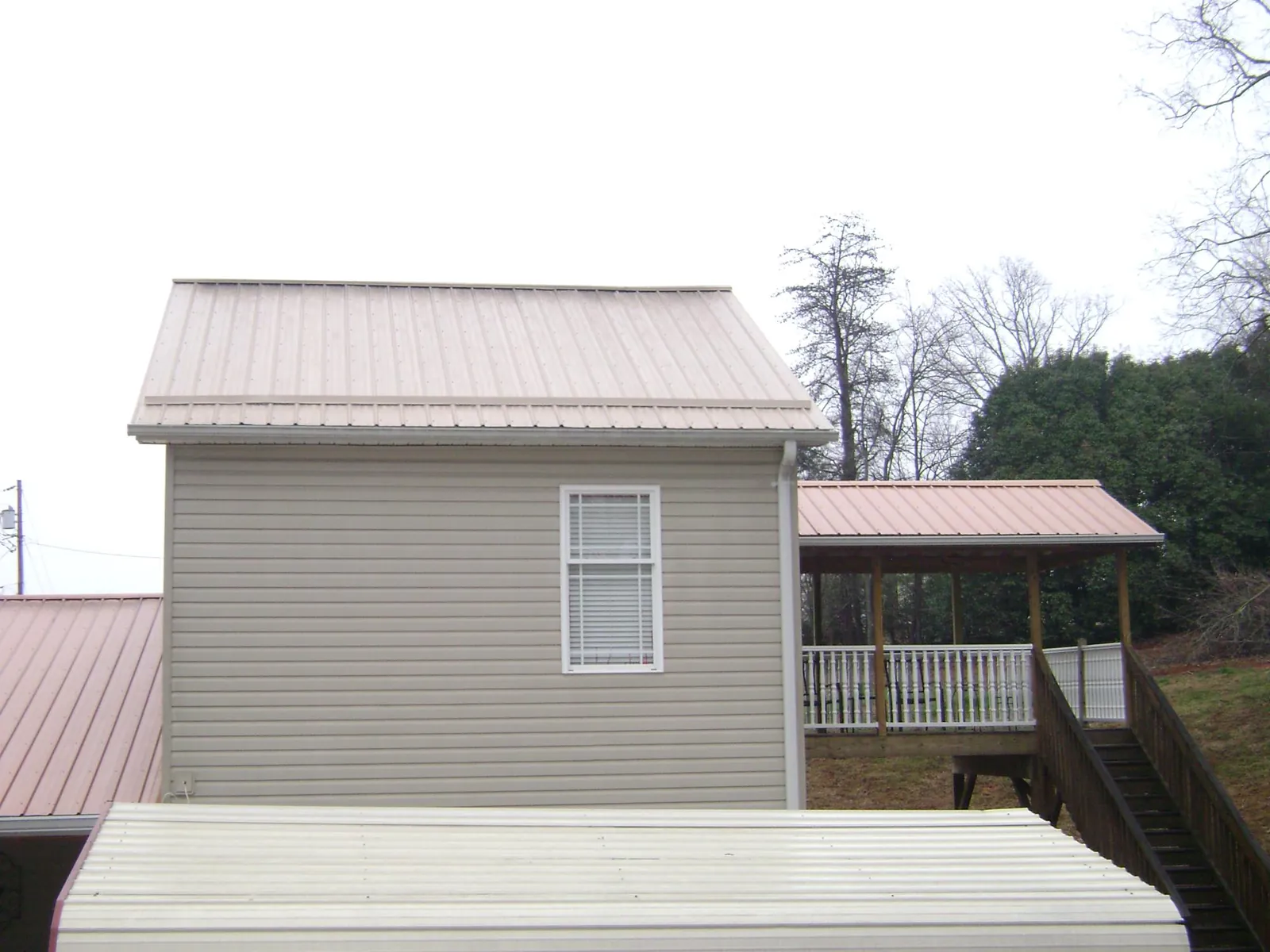 Tan metal roofs on a two story addition and attached porch, from a Roof Replacement job in Ashby